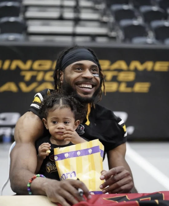 Carrington Thompson smiling while seated with a young child at an indoor football venue